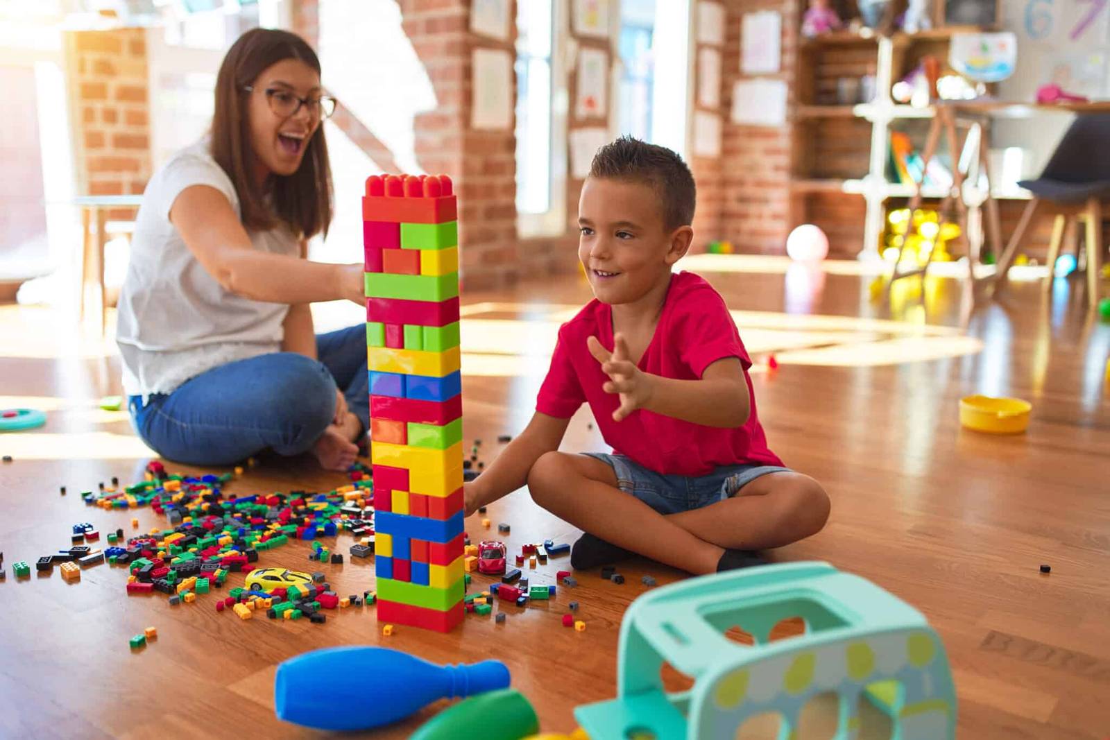 A woman and a boy building a tall block tower on the floor